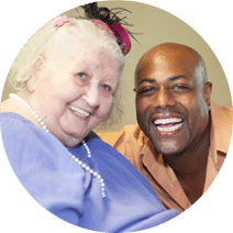Smiling man and woman, she is wearing a lavender shirt and festive pink hat